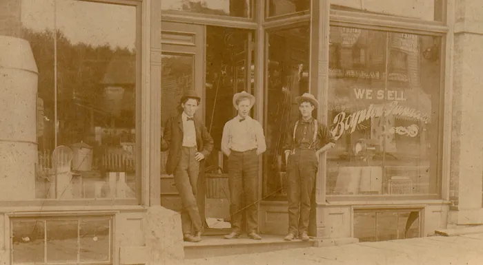 three men standing outside of store front in 1899